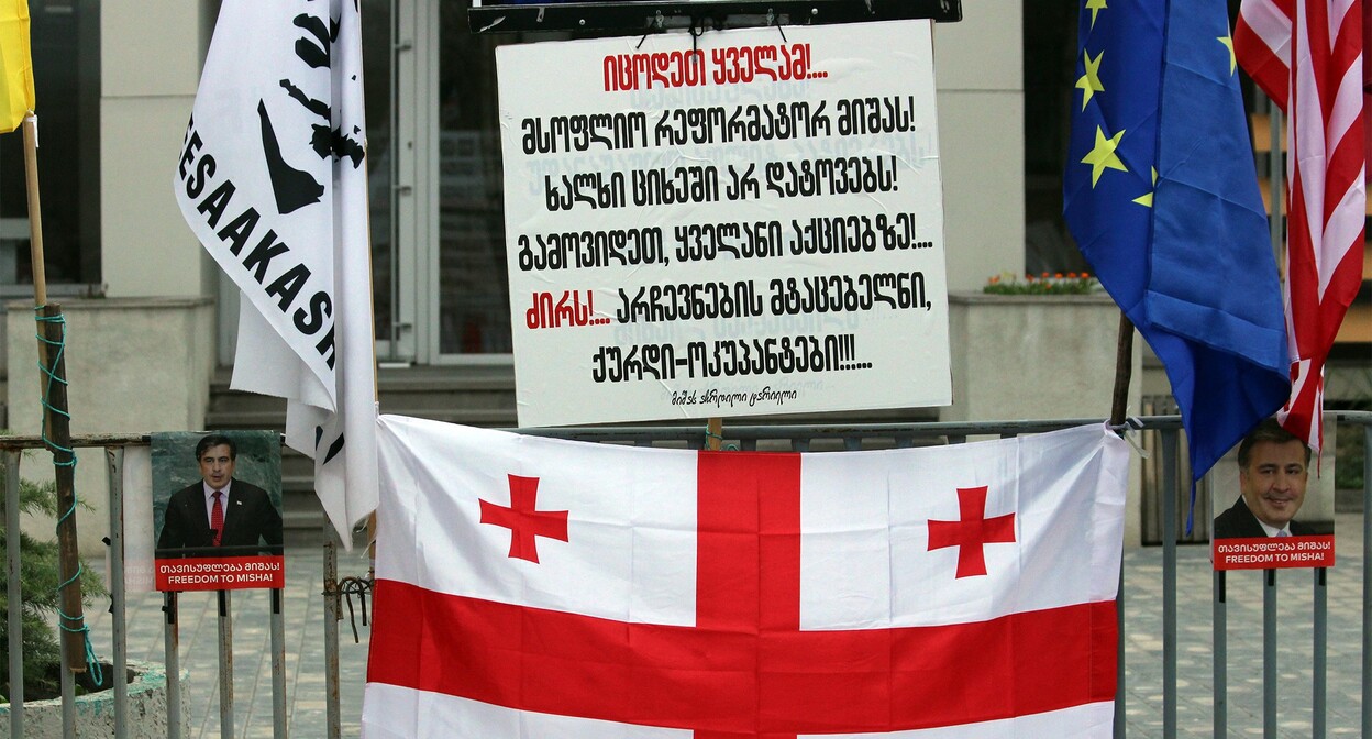 Флаг Грузии и плакат с надписью: "Знайте все! Всемирного реформатора Мишу! Народ не оставит в тюрьме! Выйдете все на акции!... Долой!... Похитителей выборов, воров-оккупантов!!!..." Фото Инны Кукуджановой для "Кавказского узла" Флаг Грузии и плакат с надписью: "Знайте все! Всемирного реформатора Мишу! Народ не оставит в тюрьме! Выйдете все на акции!... Долой!... Похитителей выборов, воров-оккупантов!!!..." Фото Инны Кукуджановой для "Кавказского узла"