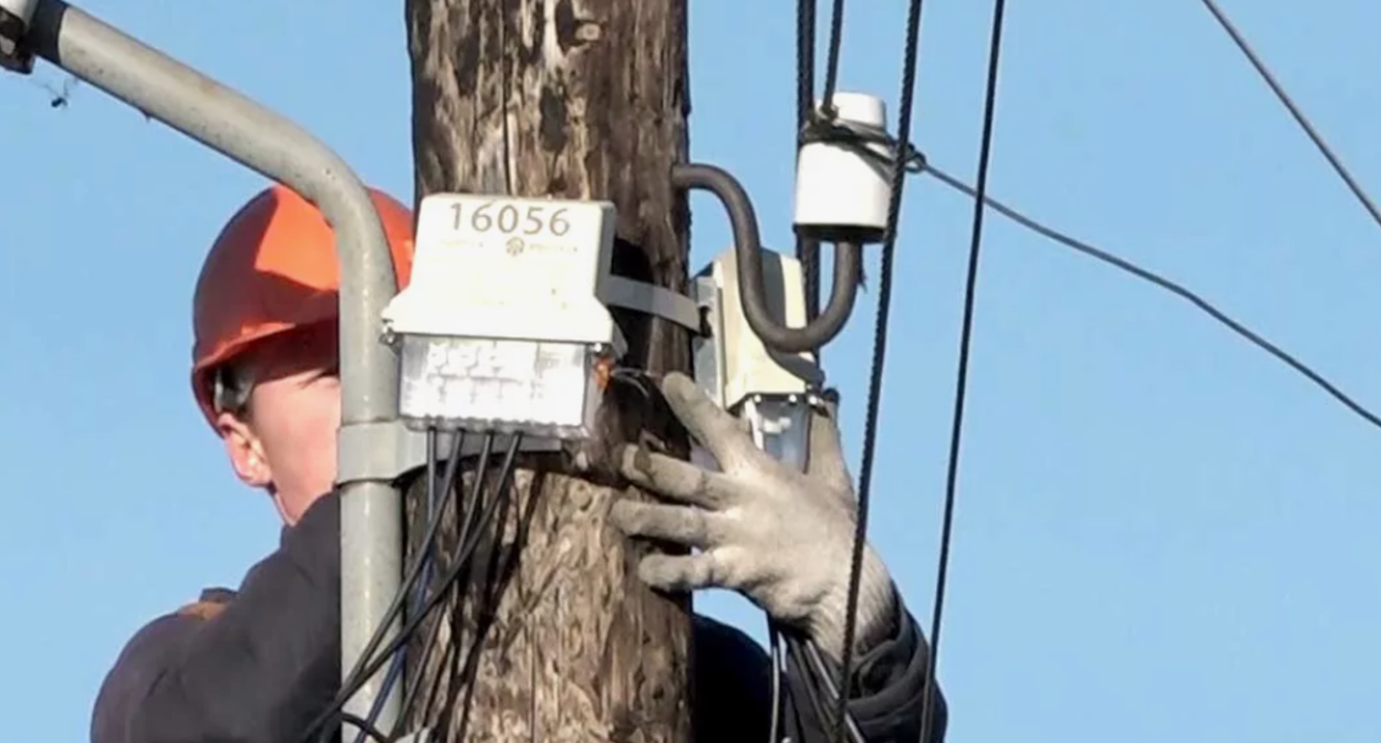 Электрик ремонтирует линию электропередачи. Скриншот фото https://dzertv.ru/tag/schetchiki/page/3/.