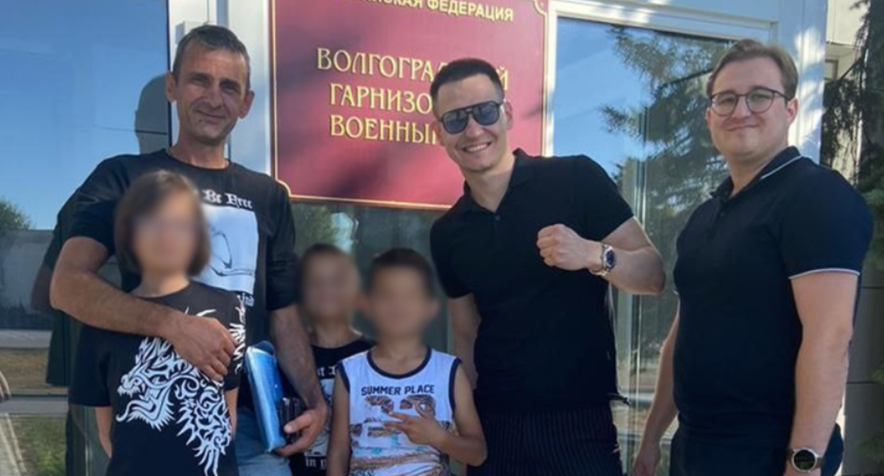 Руслан Жадаев (слева) с детьми и защитой. Скриншот фото "Высота 102" от 31.08.25, https://v102.ru/news/147301.html