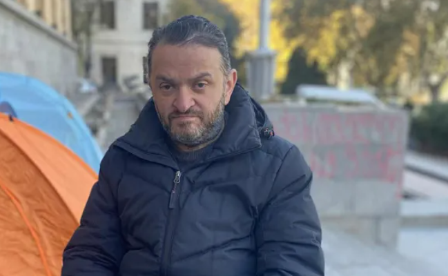 Гедеван Попхадзе. Скриншот фото "Интерпрессньюс" от 23.11.25, https://www.interpressnews.ge/ka/article/855344-gedevan-popxaze-sxva-aktivistebtan-ertad-parlamenttan-shimshilobas-27-e-dgea-ganagrzobs