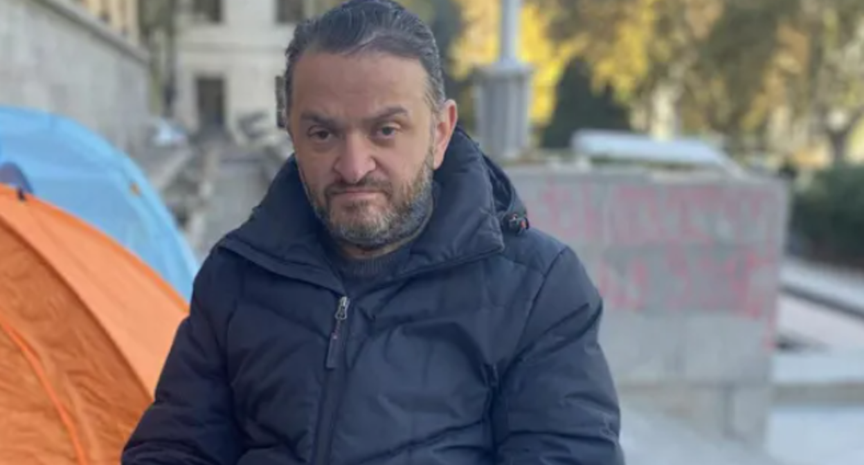 Гедеван Попхадзе. Скриншот фото "Интерпрессньюс" от 23.11.25, https://www.interpressnews.ge/ka/article/855344-gedevan-popxaze-sxva-aktivistebtan-ertad-parlamenttan-shimshilobas-27-e-dgea-ganagrzobs