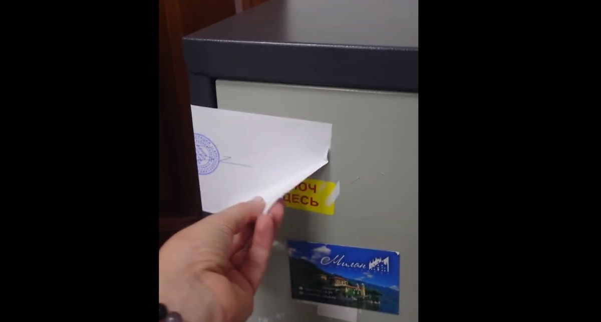 Автор видео демонстрирует отклеенный угол листа бумаги, которым опечатан сейф. Кадр видео телеграм-канала "ТИК Западная голосование 2026" https://t.me/tikzapad/91 Автор видео демонстрирует отклеенный угол листа бумаги, которым опечатан сейф. Кадр видео телеграм-канала "ТИК Западная голосование 2026" https://t.me/tikzapad/91